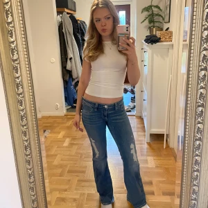 Blå bootcut jeans med slitningar - Snygga blå bootcut jeans med slitna detaljer framtill och klassiska fem fickor. Jeansen har låg midja och är tillverkade i mjukt denimtyg. Baktill finns två fickor med knappstängning och dekorativa sömmar. Dom är från gina young och är storlek M och passar mig som har S/M i jeans💕använda 2/3 gånger