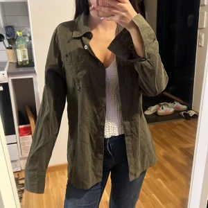 Olivgrön skjorta med knappar - Olivgrön skjorta i bomull med klassisk krage och långa ärmar. Skjortan har en bröstficka med knapp och kan bäras både öppen eller knytas framtill för en chill vibe. Snygga detaljer med knappar vid manschetterna och rak passform. Köpt från Beyond Retro men är från marie claire