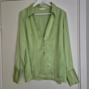 Ljusgrön skjorta/kavaj från H&M i storlek L - Satinskjorta alt tunn kavaj från H&M. Skjortan har långa ärmar med breda manschetter och knappar framtill. Tillverkad i 100% viskos.