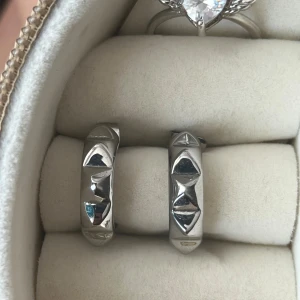 Silvriga örhängen från Goddess - Säljer ett par chunky silvriga örhängen från Goddess med coola geometriska former på ytan. De är runda hoops med en unik, kantig design som verkligen sticker ut. Perfekta för dig som vill ha något annorlunda och trendigt i smyckeskrinet.