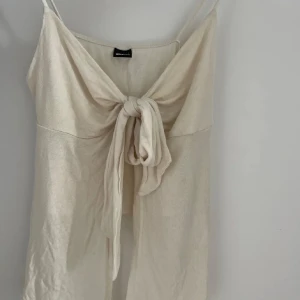 Beige linnetopp med knyt från Gina Tricot - Supersöt beige linnetopp från Gina Tricot med smala axelband och snygg knytning framtill. Toppen har en lätt och luftig känsla, perfekt för varma dagar. Stilren design som ger en chill och trendig vibe.