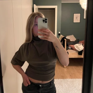 Mörkt sandfärgad  croppad topp från Gina Tricot - Topp från Gina Tricot med hög hals och korta ärmar. Toppen har en loose passform upptill och smiter åt vid midjan. Har aldrig använt, prislapp hänger kvar.