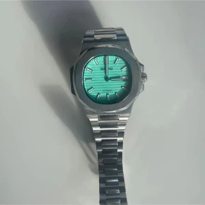  Nautilus automatisk klocka med turkos urtavla - Snygg klocka med automatisk urverk och turkos, randig urtavla. Boetten är åttakantig och armbandet är i silverfärgat metall. Index och visare är markerade i silver, och klockan har datumfunktion.