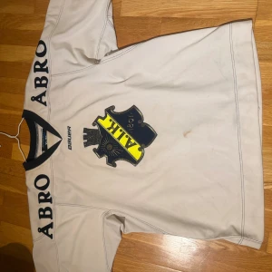 AIK hockeytröja från 2012 - AIK hockeytröja i vitt med svart och gul detalj, stor AIK-emblem på bröstet och nummer 20 på ryggen. Svart krage, svarta och gula ränder på båda armarna samt ÅBRO-tryck på axlarna. 