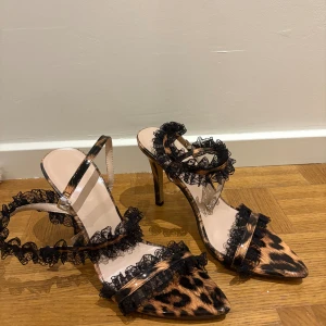 Leopardmönstrade pumps med spets - Snygga pumps med leopardmönster och spetsiga tår. Skorna har höga klackar och är dekorerade med svarta volanger i spets längs remmarna. Perfekta för dig som vill sticka ut med en unik och trendig look. Använt ett par gånger. Storlek 38