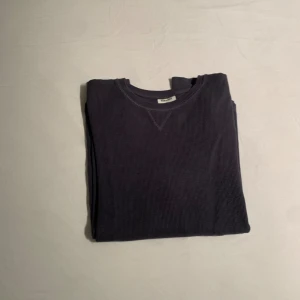 Mörkblå långärmad tröja - En stilren mörkblå långärmad i ribbad bomull. Tröjan har rund halsringning och en diskret V-detalj framtill vid halsen. Perfekt för lager-på-lager och chill vardagsstil.