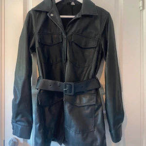 Svart skinnjacka med bälte XS - Säljer en skinnjacka i läderimitation från H&M, endast använd en gång. Jackan har en klassisk design med krage, knäppning, fyra fickor och ett justerbart skärp som kan tas bort. Denna modell säljs inte längre på H&M hemsida. Perfekt för höst och vår! Säljer den då den inte kommit till så mycket användning. Passar även någon i S.  Material:  Ytterlager: 100% polyuretan Beläggning: 100% polyuretan Foder: 100% polyester  Artikelnummer: 08842122  Vänligen läs min bio innan du gör ett köp