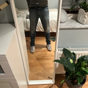 Blå Replay jeans  - Säljer ett par Replay Anbass jeans i klassisk blå denim med snyggt slitna detaljer och kontrastsömmar. Modellen har normal passform, raka ben och fem fickor. Jeansen har läderpatch bak i midjan och är tillverkade i mjukt bomullsmaterial med stretch. Storlek 31/32