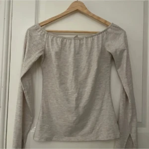 Ljusgrå offshoulder topp - Snygg ljusgrå offshoulder topp med långa ärmar. Toppen har en enkel och stilren design med lätt figurnära passform. Perfekt för dig som gillar en clean och trendig look.