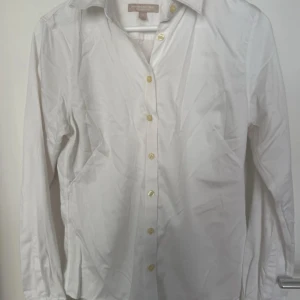 Vit skjorta från Banana Republic - Vit skjorta från Banana Republic med klassisk krage och gulfärgade knappar. Långärmad och tillverkad i mjuk bomull. Perfekt för dig som gillar en clean och stilren look. Passar dig som vill ha en enkel men snygg skjorta. Endast använd fåtalet gånger men är i bra skick. Strl 10 motsvarar ca M.