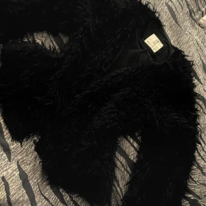 Svart pälsjacka från H&M - Fluffig svart pälsjacka från H&M med lång ärm och klassisk krage. Jackan har en cool, oversized look och är tillverkad i syntetmaterial som ger en mjuk och lyxig känsla. Perfekt för dig som vill sticka ut och hålla värmen under kyliga dagar.Det står de 12/14 år men hade sagt de XS.