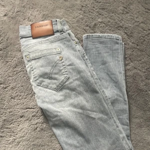 Grå skinny jeans från Dondup - Snygga ljusgrå jeans från Dondup med slitningar på benen för en cool look. Modellen är skinny med klassisk femficksdesign och detaljer i silver. Jeansen har normal passform och är tillverkade i mjukt denimtyg.