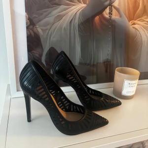 Svarta pumps med spetsig tå - Snygga svarta pumps med spetsig tå och hög klack. Skorna har ett mönster i mesh och skinn som ger en modern och edgy look. Perfekta för dig som vill sticka ut med stilrena detaljer och en elegant siluett.