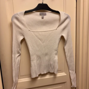 Vit ribbad långärmad topp H&M Stl XS - Snygg vit ribbad topp från H&M med lång ärm och fyrkantig urringning. Modellen är figurnära och har en stilren look med diskret struktur i materialet. Passar storlek XS.