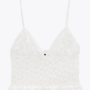 Vit broderad linnetopp från Zara - Supersöt vit linnetopp från Zara med smala axelband, v-ringning och broderade blommor. Toppen har smockad midja och volangkant nedtill för en romantisk vibe. Perfekt till sommarens alla outfits! Säljer då den tyvärr är för liten! Endast använd 1 gång🩷