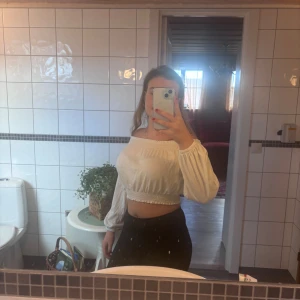 Offshoulder croppad topp i vit - Superfin croppad offshoulder topp i vit med långa puffiga ärmar och smockdetaljer vid halsringning och midja. Perfekt för dig som gillar romantisk och trendig stil. Tunn och luftig, passar till både jeans och kjol.