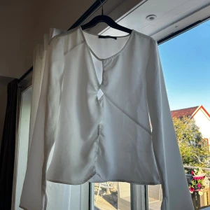 Vit omlottblus med lång ärm - Säljer en stilren vit omlottblus från BikBok. Blusen har lång ärm, rund halsringning och en snygg omlottdetalj framtill. Materialet är lätt och har en satinliknande finish som ger en elegant känsla. Perfekt att styla med jeans eller kjol. Finns en enda defekt (sista bild)