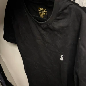 Svart t-shirt från Polo Ralph Lauren - Svart t-shirt från Polo Ralph Lauren med klassisk vit broderad logga på bröstet. Modellen är custom slim fit och har rund halsringning och korta ärmar. Tillverkad i mjuk bomull för en skön känsla. Skriv för fler bilder!!