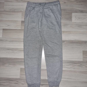 Grå mjukisbyxor från Calliope M - Grå mjukisbyxor från Calliope i storlek M,  uppleverdesmåistorleken. Byxorna har resår i midjan med snörning, två sidofickor och muddar vid bensluten. De har ett litet hål i rumpan, se bild. Perfekta för chill dagar eller när du vill vara extra bekväm.