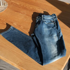 Replay Hyperflex Anbass Mörkblå - Snygga blå jeans från Replay med en klassisk femficksdesign och lätt slitna detaljer. De har en knappgylf och är perfekta för en avslappnad stil. Märkesloggan syns på bakfickan. Endast använda 1-2 gånger.