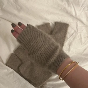 Beige stickade fingerlösa handskar - Säljer ett par beige stickade fingerlösa handskar som är perfekta för dig som vill ha värme men ändå kunna använda mobilen eller fixa med småsaker. De har en enkel och clean design med ribbad kant vid handleden. Passar dig som gillar en chill och stilren look.