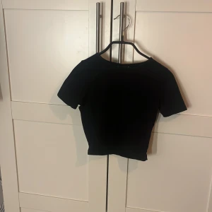 Svart croppad topp från ASOS DESIGN - Svart croppad topp från ASOS DESIGN med rund hals och korta ärmar. Enkel och stilren design som är lätt att matcha. Mjuk och stretchig kvalitet som sitter snyggt och bekvämt. Perfekt för dig som gillar minimalistisk stil.