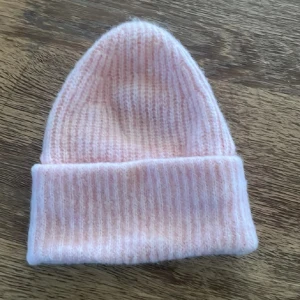 Ljusrosa ribbad ullmössa 52/54 - Mysig ljusrosa mössa i ribbstickad ullblandning. Klassisk beanie-modell med uppvikt kant, perfekt för kyliga dagar. Snygg och enkel att matcha med olika outfits.