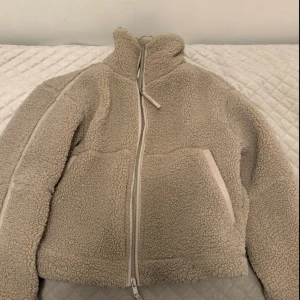 Teddyjacka från H&M - Teddyjacka som knappt är använd, säljer den efter eftersom att den inte kommer till nån användning.  Beige teddyjacka med hög krage och tvåvägsdragkedja framtill. Jackan har två stora fickor och en oversized passform som ger en chill vibe. Perfekt för kalla dagar när du vill vara både varm och snygg. Fodrad insida och mjukt teddy-material. Pris kan diskuteras!  Du står för frakten