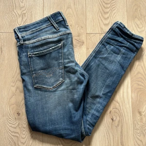 Replay Anbass slim fit jeans blå - Snygga blå Replay Anbass jeans i slim fit med snygga slitningar. Modellen är Anbass Aged 5 years och är i storleken W32 L30. Byxorna är i bra skick! Tveka inte på att höra av dig om du har frågor!