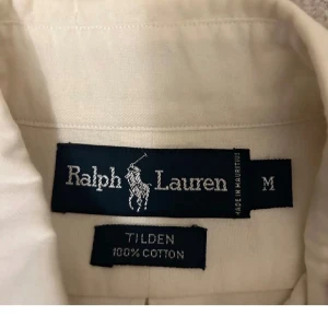 Vit skjorta från Ralph Lauren - Klassisk vit skjorta från Ralph Lauren med button-down krage och broderad logga på bröstfickan. Skjortan är tillverkad i 100% bomull och har knappar framtill. Perfekt för en clean och stilren look.
