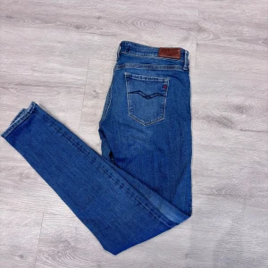 Blå Replay jeans, midwaist, storlek 29/32 - Snygga blå jeans från Replay med klassisk femficksdesign och läderpatch bak. Jeansen har en smal passform och normal midja. Materialet är mjukt denim i bomull med lite stretch för extra komfort. Perfekta för dig som gillar stilrena och tidlösa jeans.