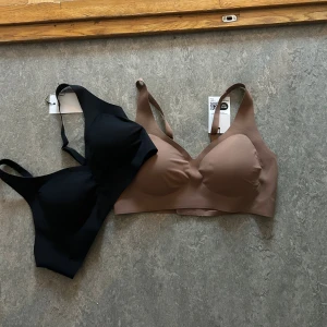 Svart och brun sömlös BH topp - Två stilrena sömlösa linnetoppar i svart och brun. De har breda axelband och mjuk, stretchig passform som ger en clean look under kläderna. Perfekta för dig som vill ha en enkel och bekväm topp till vardags.