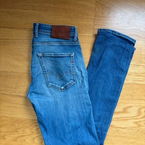 Blå Replay jeans med smal passform - Säljer ett par snygga blå jeans från Replay med klassisk femficksdesign och ljusa slitningar framtill. Jeansen har normal midja och smal passform, perfekt till vardagslooken. Materialet är mjukt jeans i bomull och de har en stilren läderpatch bak i midjan. Nypris 1500 mitt pris 249kr. Priset är ej hugget i sten. Hör av er vid minsta lilla fundering. 