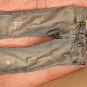 Replay ljusblå slitna jeans - Säljer ett par ljusblå jeans från Replay med slitna detaljer och hål på framsidan. Jeansen har klassisk femficksdesign, dragkedja och knapp, samt en snygg tvättad look. Perfekta för dig som gillar en avslappnad och trendig stil.