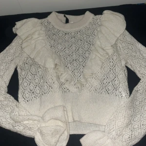 Vit stickad volangtröja Divided - Supersöt vit stickad tröja från Divided med volanger framtill och genombrutet mönster. Tröjan har långa ärmar och ribbade muddar. Perfekt för dig som gillar romantisk och trendig stil.