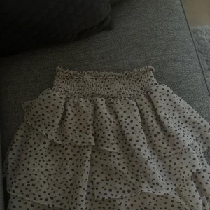 Prickig volangkjol med resårmidja - Supersöt kortkjol med volanger och resår i midjan från H&M. Kjolen är vit med svarta prickar och har en luftig känsla, perfekt för varma dagar. Den har flera lager volanger som ger en cool look🤍