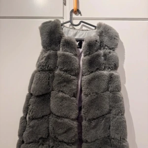 Grå fluffig pälsväst från YXFS - Supermjuk och fluffig grå pälsväst från YXFS. Västen har en chunky look med breda paneler och är tillverkad i syntetpäls med insida i polyester. Perfekt för att ge din outfit en extra edge och värme under kyliga dagar.