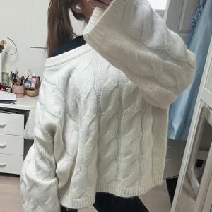 stickad tröja - Säljer en supermysig vit stickad tröja med grova kabelstickade detaljer och breda ärmar. Tröjan har en loose och oversized passform, perfekt för att chilla eller hänga med kompisar. Den har en bred halsringning och är riktigt skön att bära under kyliga dagar.