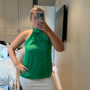 Grön omlott linnetopp från Amisu - Snygg grön linnetopp från Amisu i storlek S. Toppen har hög hals med omlott och knyt i nacken, vilket ger en cool detalj baktill. Materialet är glansigt och känns lätt mot huden, perfekt för varma dagar. Ärmlös och loose fit för en chill vibe.