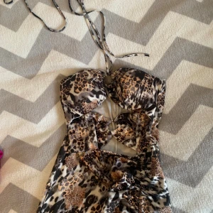 Leopardmönstrad långklänning med snörning - Snygg långklänning med leopardmönster och coola cut-outs framtill. Klänningen har snörning i halsen och en figurnära passform. Perfekt för dig som vill sticka ut med ett djurmönster och trendiga detaljer.