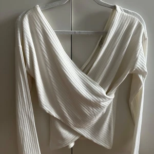 Vit omlottopp med ribbad struktur - Säljer en vit långärmad omlottopp med ribbad struktur. Toppen har en djup v-ringning. Perfekt att styla med jeans eller kjol för en trendig look