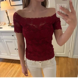Offshoulder spetstopp - Snygg vinröd topp med offshoulder-modell och korta ärmar. Hela toppen är täckt av vacker spets med blommigt mönster och har en feminin, figurnära passform. Perfekt för dig som vill sticka ut lite extra.