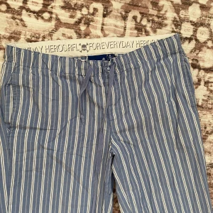 Randiga blå pyjamasbyxor  - Blå pyjamasbyxor med vita vertikala ränder från RFL. Byxorna har elastisk midja med snörning och raka ben. Perfekta för chill dagar eller när du vill ha en avslappnad look. Lätta och luftiga i materialet.💛