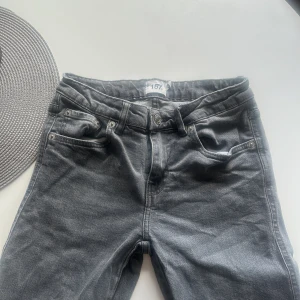 Grå jeansbyxor från 157, XS - Snygga grå jeansbyxor från Lager 157 i storlek XS. Klassisk femficksmodell med silverfärgade nitar och knappar, samt bakfickor med lock och knapp. Full längd och bälteshällor, perfekt till sneakers eller boots.Tyvärr har dom slitits lite längst ner. Säljer för dom har blivit för små för mig.