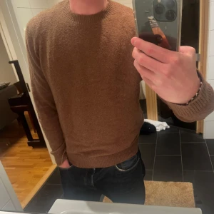 Brun stickad tröja  - Mysig brun stickad tröja från THESE GLORY DAYS med rund halsringning och ribbade muddar. Perfekt för kyliga dagar och enkel att matcha med jeans eller chinos. Klassisk och stilren modell som funkar till det mesta.