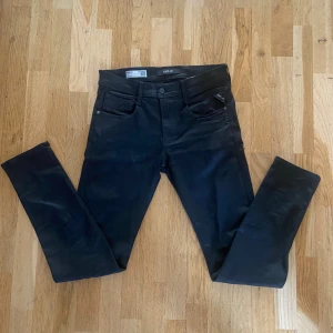 Svarta Replay Anbass jeans herr - Svarta Replay Anbass jeans med slim passform och klassisk femficksdesign. Jeansen har en snygg, stilren look med svarta sömmar och diskret Replay-logga på fickan. Materialet är stretchigt och bekvämt, perfekt för en modern och clean stil. Obs Den har ett litet hål som man ser vid bild 2 vid vänstra benet därav priset annars är den perfekta Storlek 30🤩 Ny pris~1200 Mitt pris 400