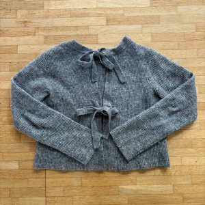 Grå stickad kofta med knyt från Object - Supersöt grå ribbstickad kofta från Object med två knytband framtill. Koftan har lång ärm och en rak, lite boxig passform. Perfekt för lager-på-lager och chill dagar. Koftan har blivit lite nopprig och är lite sticksig i materialet men är i sin helhet fortfarande fin.