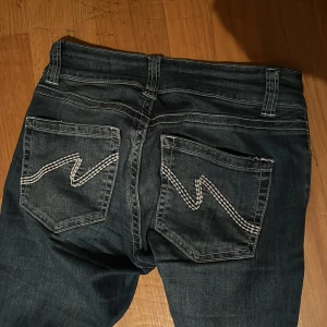 Blå bootcut jeans från Nelly, stl 34 - Snygga blå bootcut jeans från Nelly med coola kontrastsömmar och broderade bakfickor. Jeansen har låg midja och klassisk femficksdesign. Perfekta för dig som gillar en retro vibe och vill sticka ut lite extra.