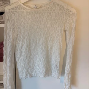 Vit spetsblus från H&M - Säljer en vit långärmad blus från H&M i genombruten spets med snyggt mönster. Toppen har rund halsringning och är figurnära med transparent känsla, perfekt för att styla lager på lager. Superfin till jeans eller kjol för en trendig look.