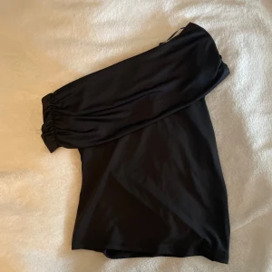 Svart one shoulder topp  - Snygg svart topp med one shoulder-design. Toppen är figurnära och har en stilren look som passar perfekt till jeans eller kjol. Tillverkad i ett mjukt och stretchigt material för extra komfort.